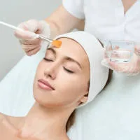 Kosmetolog nakłada pędzelkiem peeling chemiczny na twarz klientki w Prestige Laser we Wrocławiu.