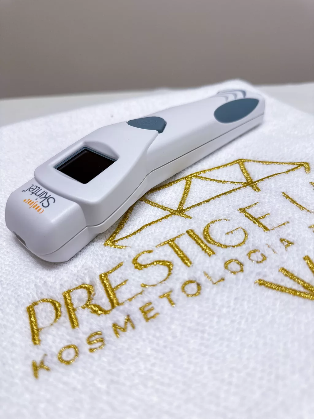 Czytnik Skintel leżący na białym ręczniku z haftowanym logo gabinetu kosmetologicznego Prestige Laser we Wrocławiu.