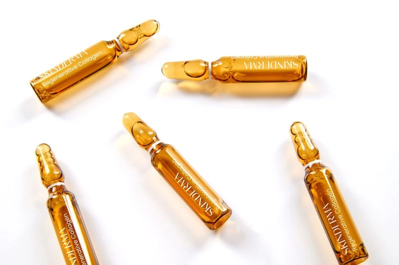 Pięć bursztynowych ampułek z kolagenem regenerującym Skinderma leży na białym tle, ułożonych w różnych kierunkach.