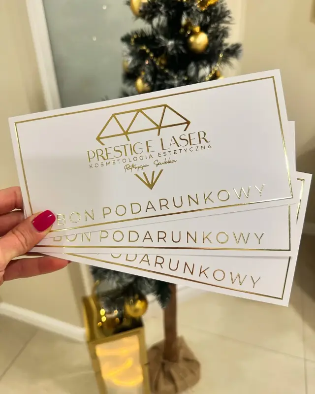 Trzy bony podarunkowe do salonu kosmetycznego Prestigelaser, w tle ozdobiona choinka.